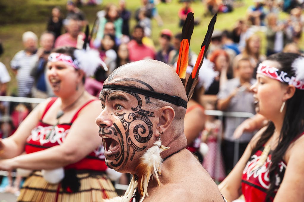 An energetic Maori performer with a painted face during a tribal festival in daylight.