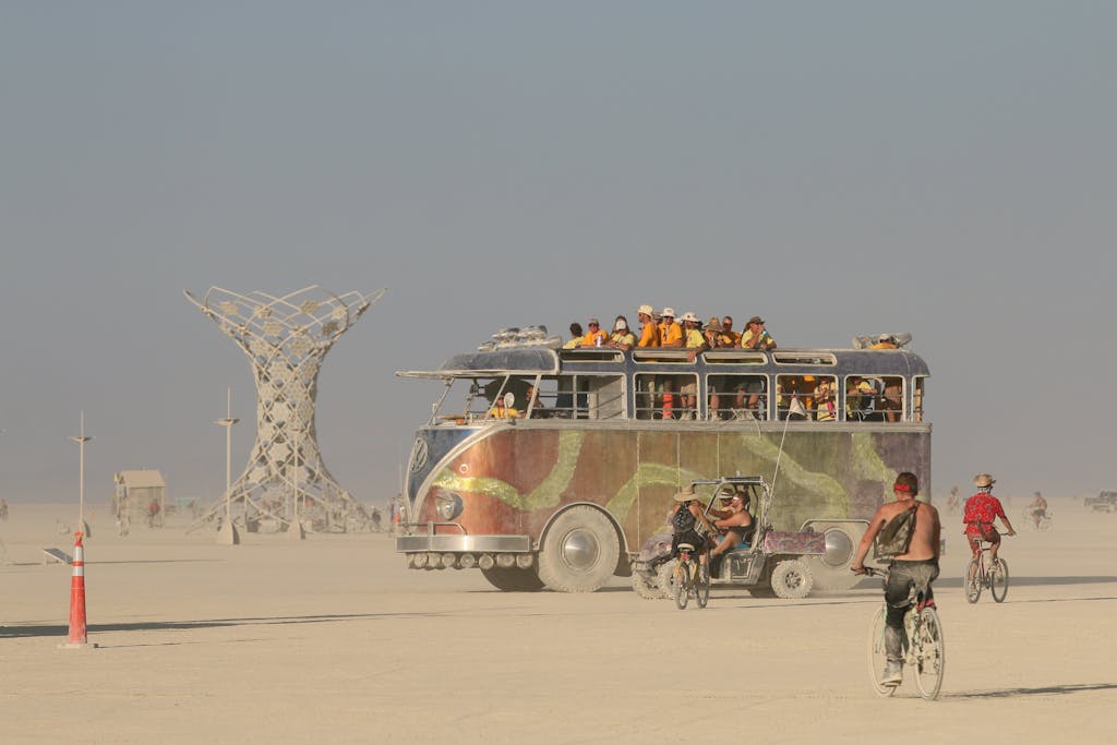 An artistic vehicle and cyclists traverse the desert at Burning Man Festival.