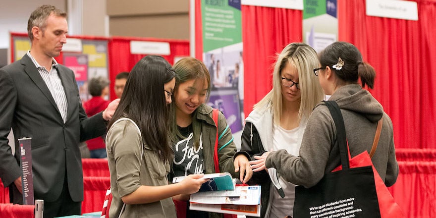 Young female participants at an education fair having a discussion while looking at a brochure