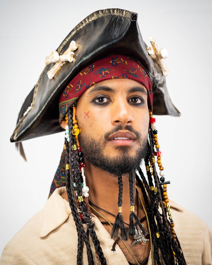Close-up portrait of a man in pirate costume with beaded hair and tricorn hat.