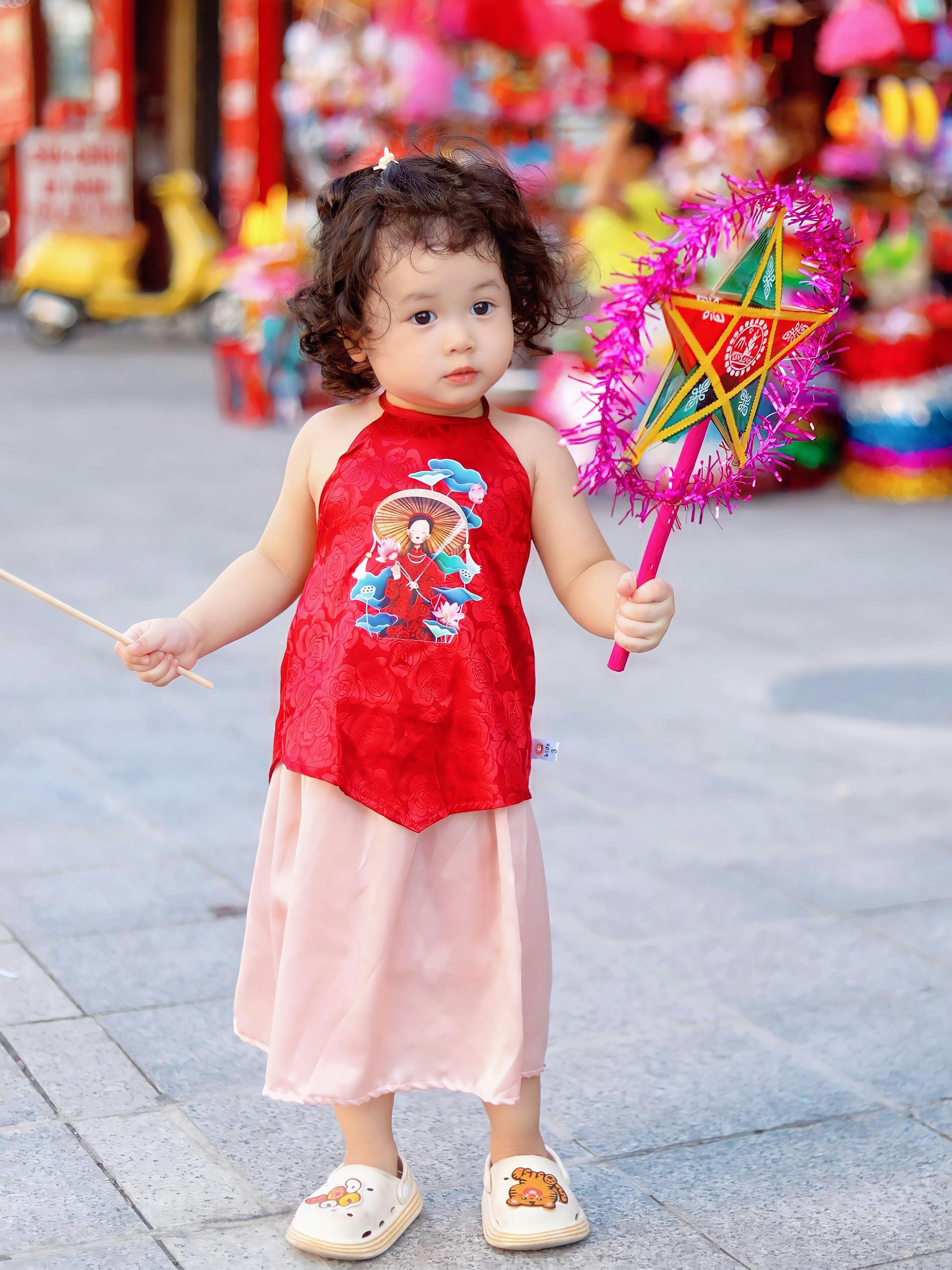 Cute child holding a traditional lantern during Moon Festival on city streets. Joyful moment captured outdoors.