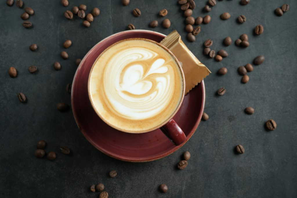 A cup of cappuccino on a saucer surrounded by coffee beans