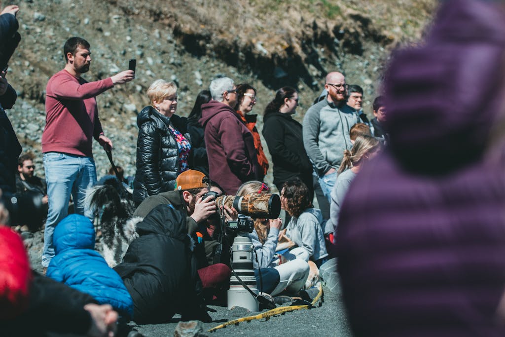 Group of people gathered outdoors, some taking photos and observing an event.