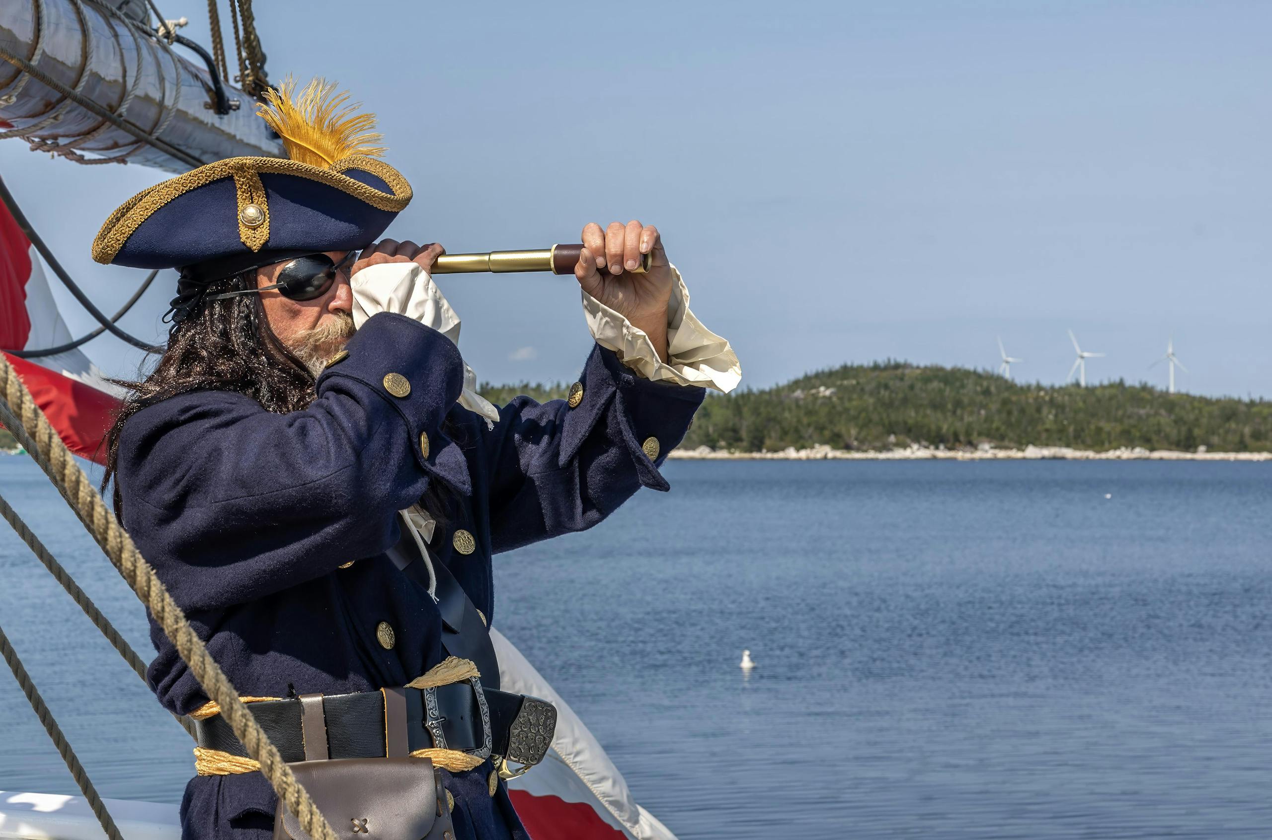 Pirate in blue outfit looking through spyglass on ship by the sea.