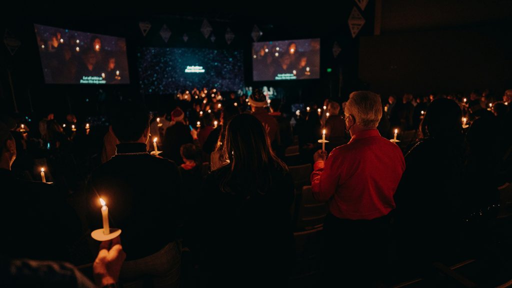 Packed church at midnight on Christmas Eve. Hundreds of candles, wide angle showing scale and atmosphere.