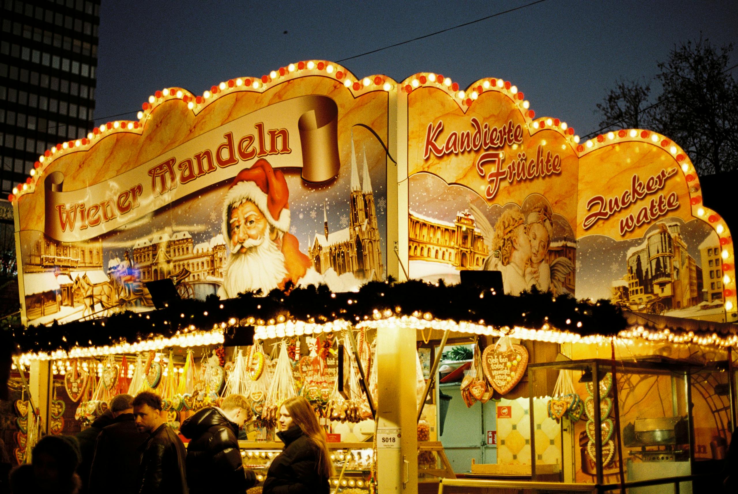 Illuminated Christmas market stall in Berlin showcasing traditional sweets and festive decor.