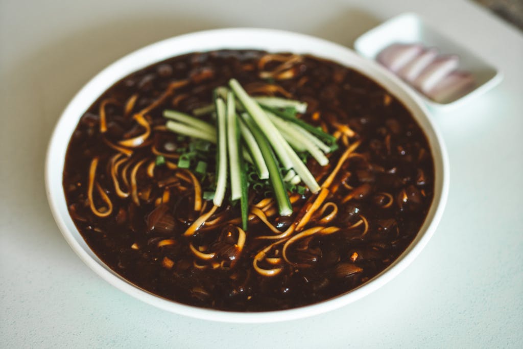 Delicious bowl of Jajangmyeon, a Korean-Chinese dish with savory black bean sauce and fresh cucumber garnishing.