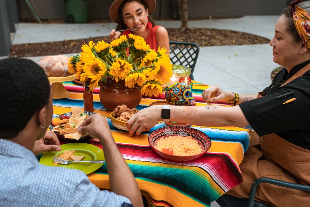 Group of adults enjoying a colorful outdoor meal with sunflowers on the table.