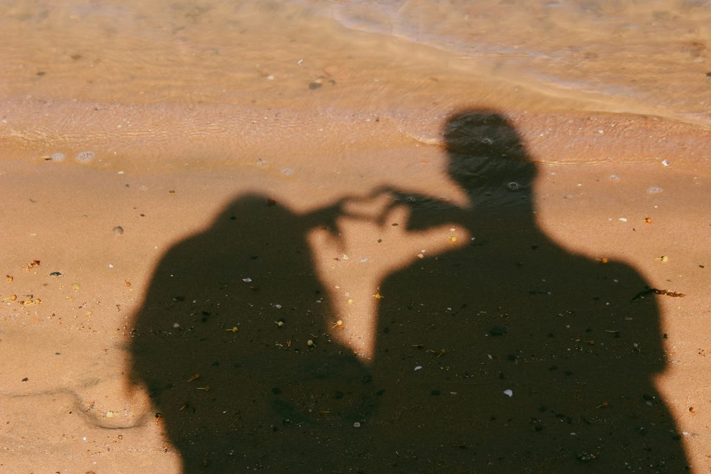 A shadow of a man and a woman making a love heart sign with their hands on the sand at the beach 