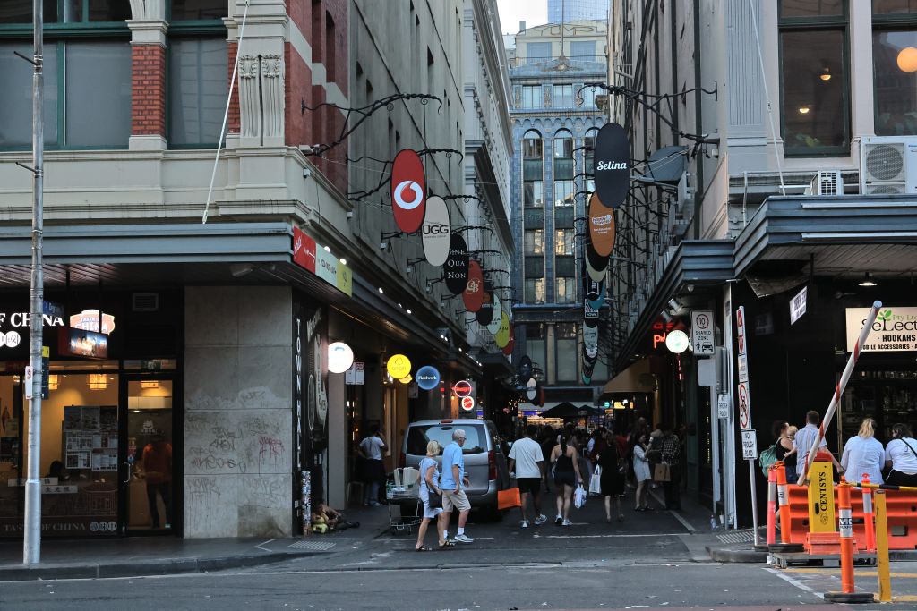 A bustling laneway in Melbourne, Australia with people shopping and iconic signage.