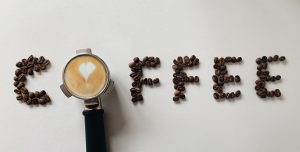 Artistic arrangement of coffee beans spelling 'coffee' with a portafilter and latte art heart.