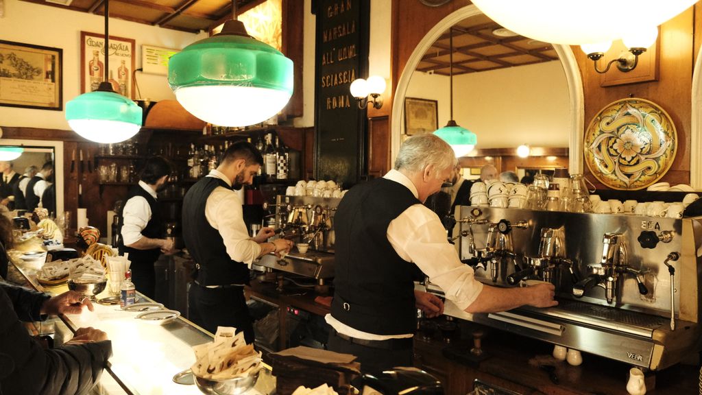 Baristas prepare coffee in a classic Italian café with vintage decor.