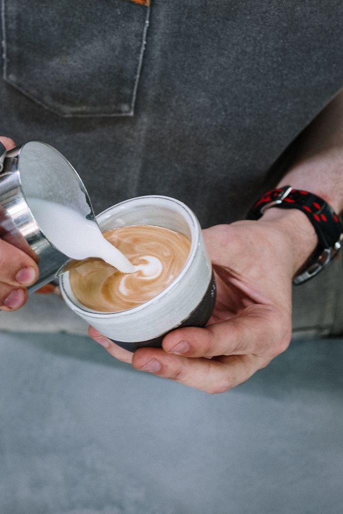 Close-up of a barista pouring milk to create latte art in a cozy café setting.