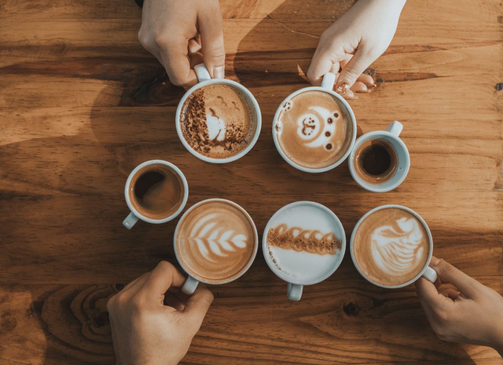 Creative latte art designs on multiple coffee cups arranged on a wooden table, captured from above.