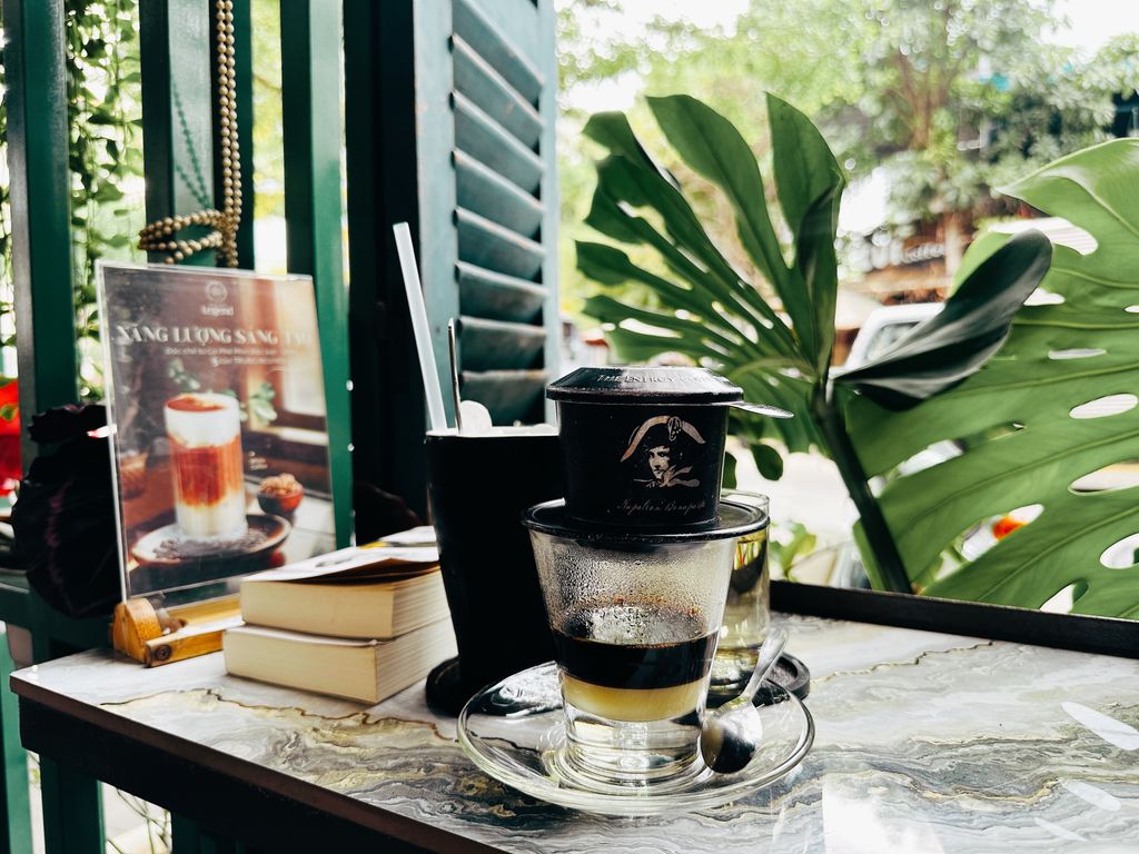 Refreshing Vietnamese coffee in a glass with a phin filter, set on a café table surrounded by tropical plants.
